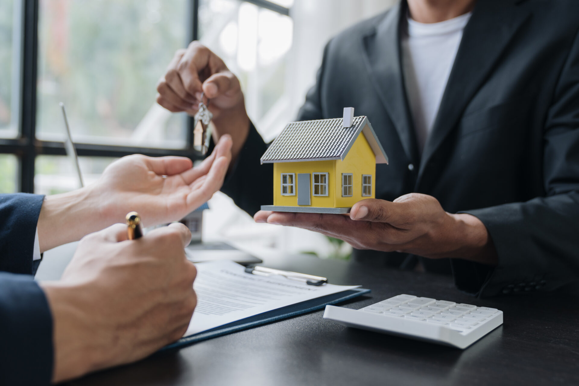 A man is holding a house model while two other people are sitting at the table.